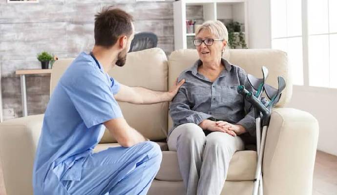 Male Health Visitor Nursing Home Talking With Retired Old Woman While Sitting Couch Old Woman With Crutches